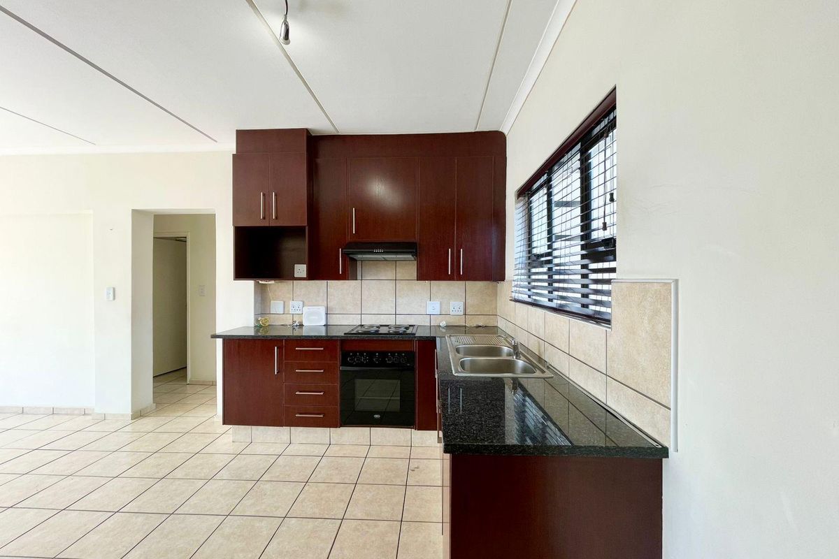 A clean, functional kitchen featuring dark wood cabinetry, granite countertops, built-in oven, hob, extractor fan, and tiled flooring.