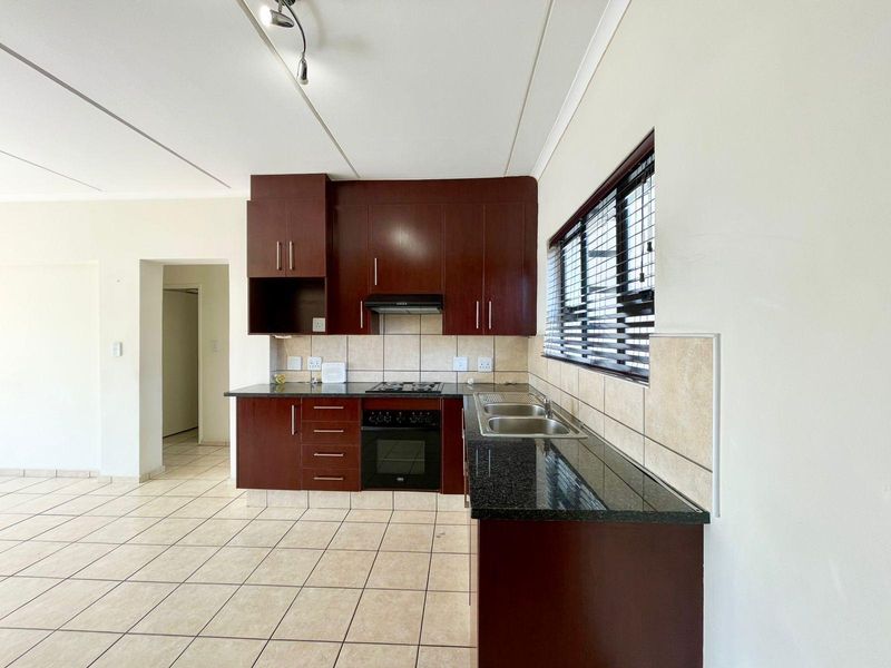 A clean, functional kitchen featuring dark wood cabinetry, granite countertops, built-in oven, hob, extractor fan, and tiled flooring.