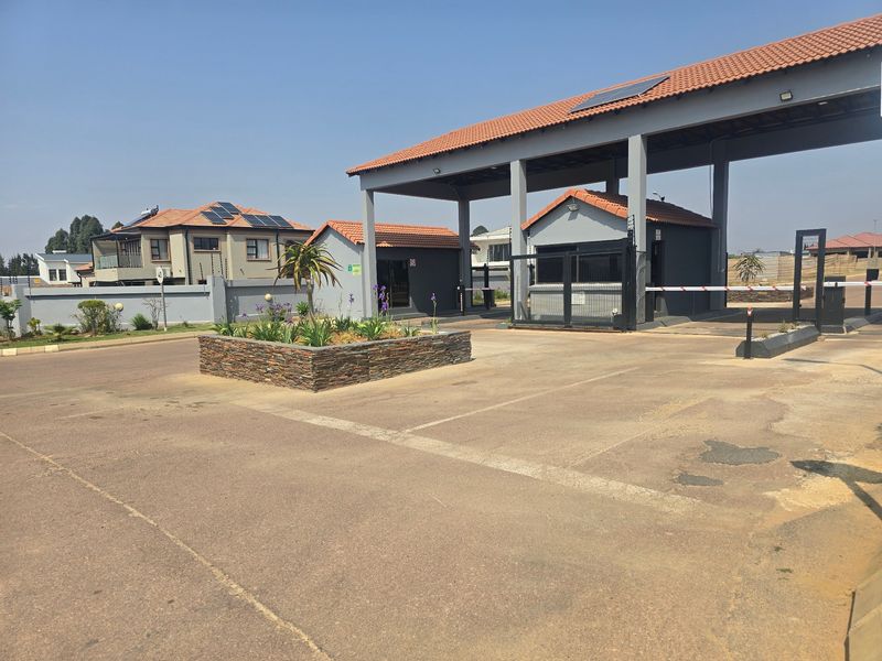 The entrance to the residential estate features a secure gatehouse, boom gate access, paved driveway, and well-maintained perimeter walling with electric fencing.