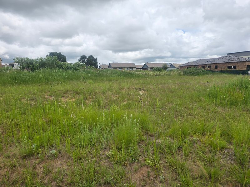 A view of a vacant residential plot featuring natural grassland with surrounding residential development in the background.
