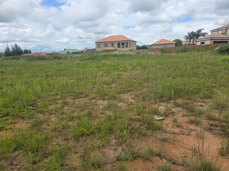 A view of a vacant residential plot of land with natural grass cover, situated in a developed suburban neighborhood.