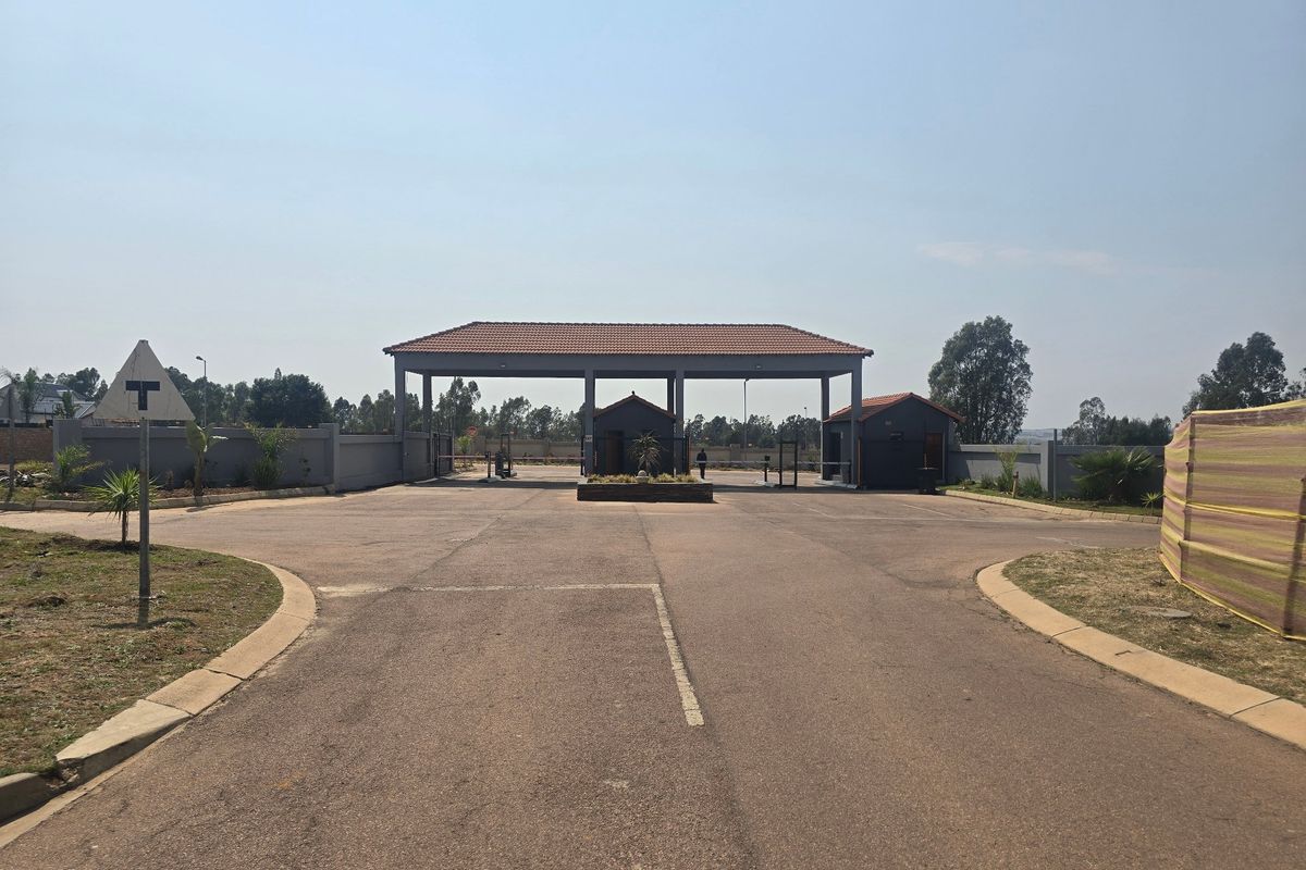 A view of the secure gated entrance to the residential estate, featuring a paved driveway and established perimeter walling.