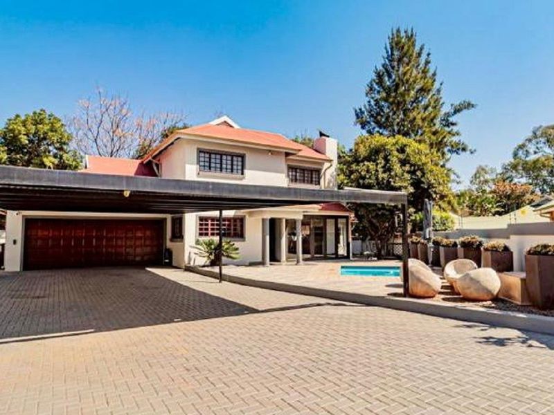 Spacious front exterior featuring a large paved driveway, integrated carport, swimming pool, and a well-maintained two-story residential building.