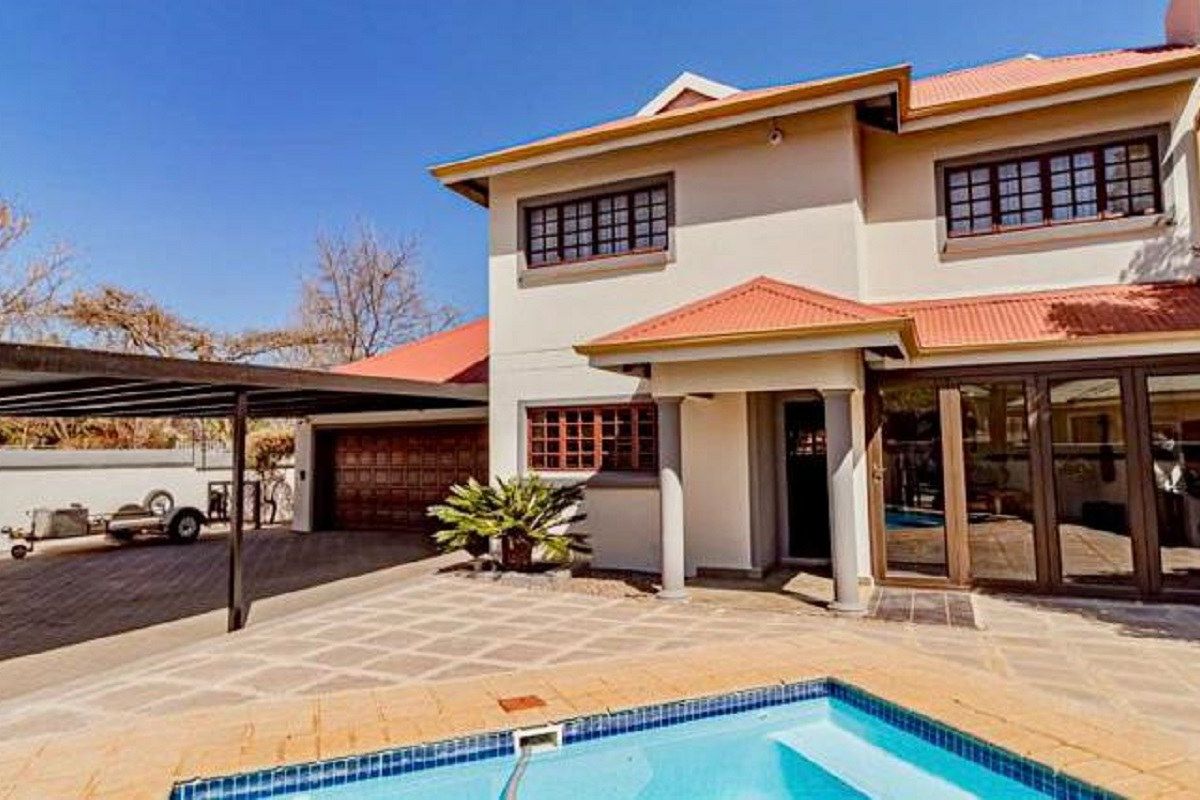 Rear view of the house featuring a swimming pool, paved patio area, attached carport, and multi-level facade with tiled roofing.