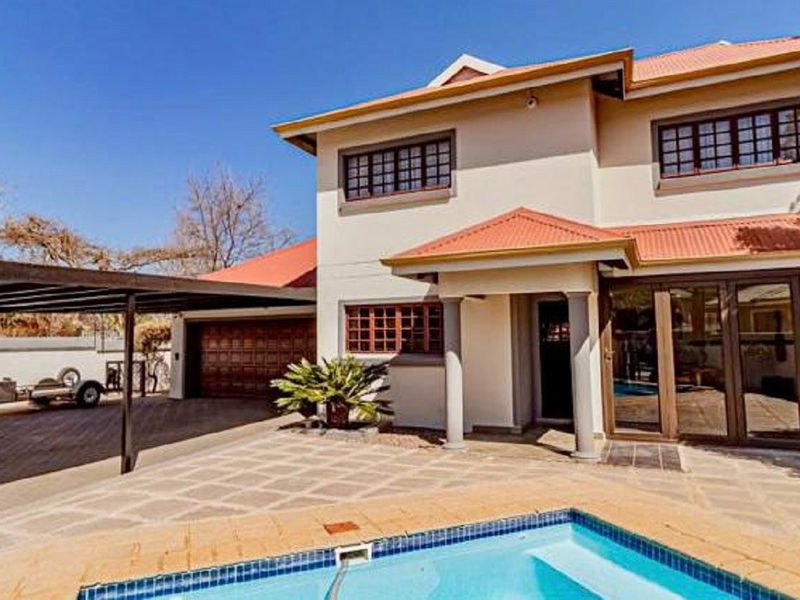 Rear view of the house featuring a swimming pool, paved patio area, attached carport, and multi-level facade with tiled roofing.