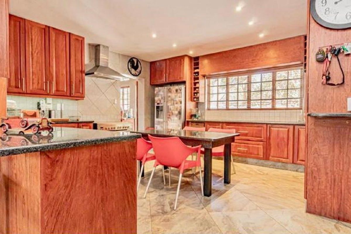 Spacious kitchen featuring warm-toned wooden cabinetry, granite countertops, tiled flooring, and integrated lighting, offering a functional layout with ample storage space.