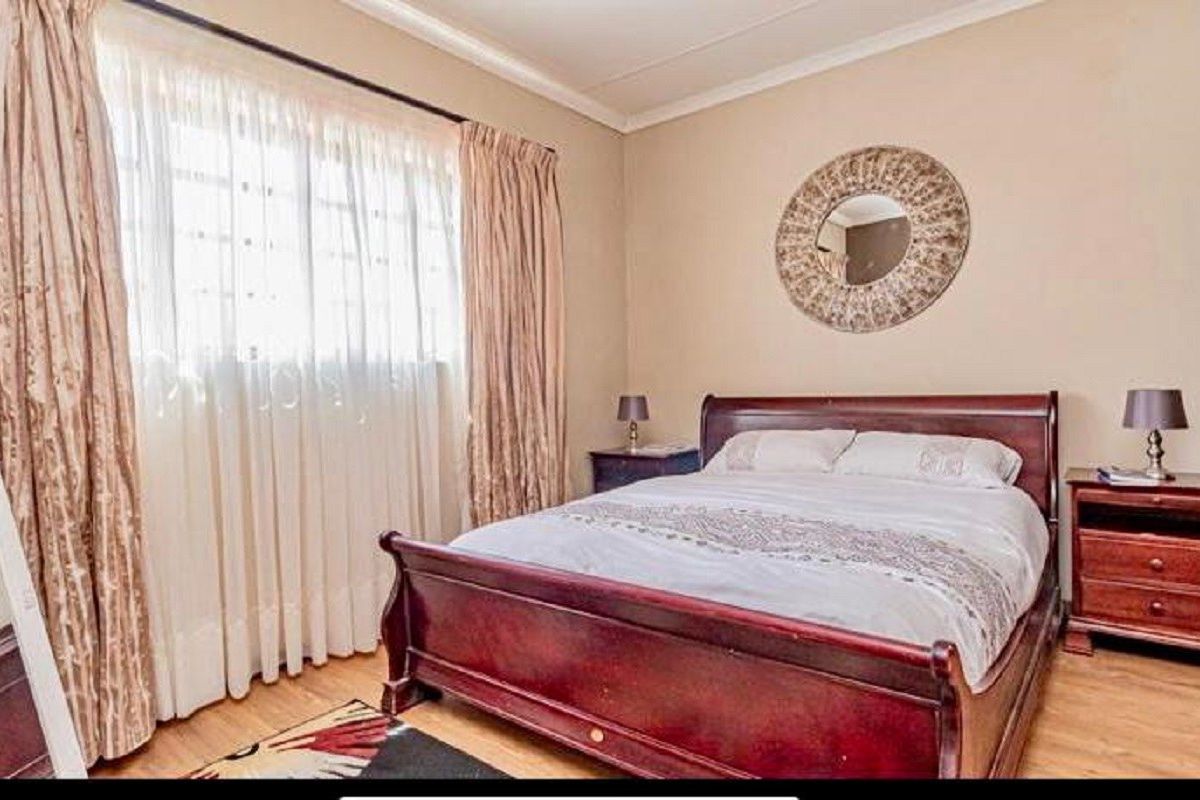 A well-maintained bedroom featuring laminate flooring, neutral wall tones, and large windows with curtain treatments, offering a comfortable and functional living space.