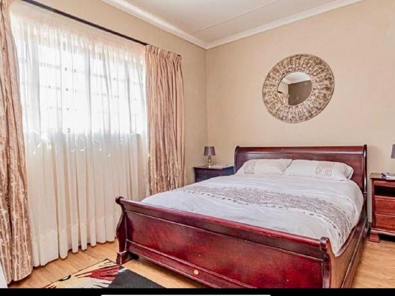 A well-maintained bedroom featuring laminate flooring, neutral wall tones, and large windows with curtain treatments, offering a comfortable and functional living space.