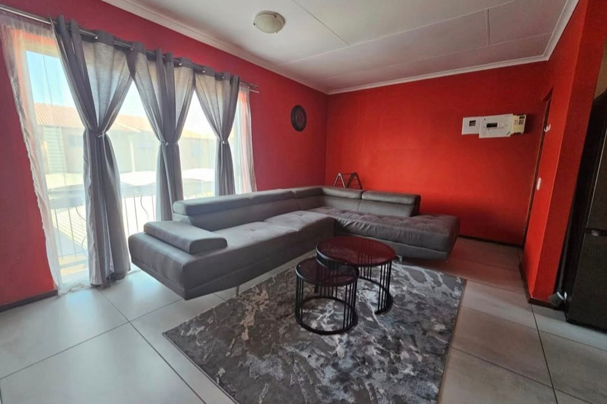A living room featuring large format floor tiles, a sliding glass door providing natural light, and a wall-mounted air conditioning unit.