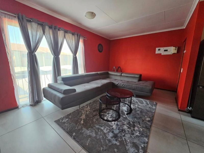 A living room featuring large format floor tiles, a sliding glass door providing natural light, and a wall-mounted air conditioning unit.
