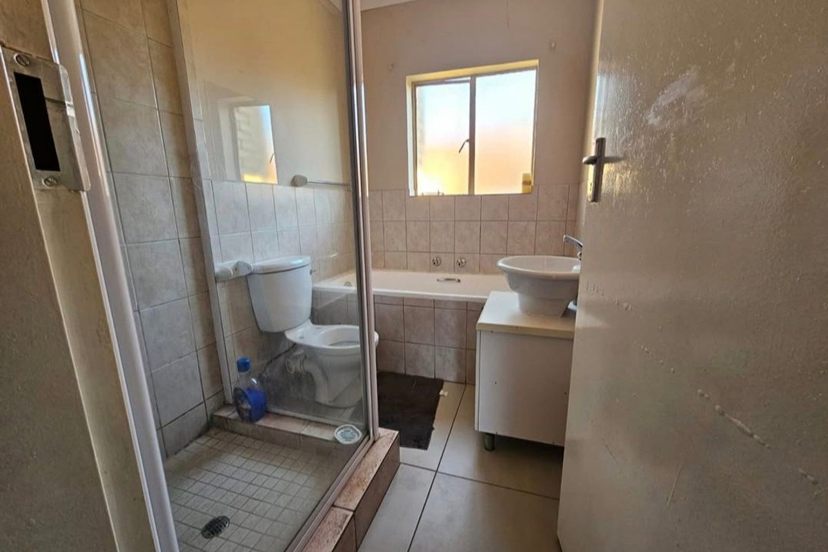 A functional bathroom featuring a shower enclosure, bathtub, and pedestal basin with neutral wall and floor tiling.