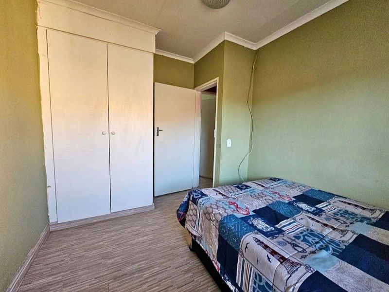 A bedroom featuring built-in wardrobes, laminate flooring, and cove cornicing, requiring minor cosmetic updates to the wall finishes.
