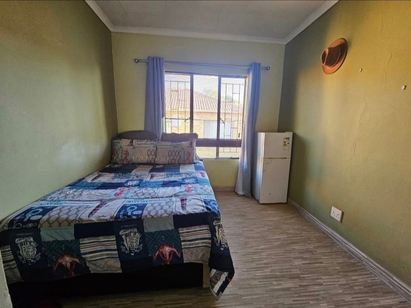A bedroom featuring laminate flooring and security bars on the window. The room requires cosmetic updates including wall repairs and fresh paint.