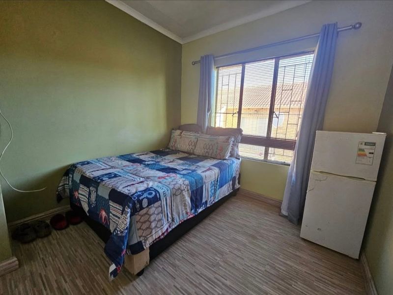 A functional bedroom featuring laminate flooring, a window with security bars, and neutral wall finishes, offering a practical space for residents.