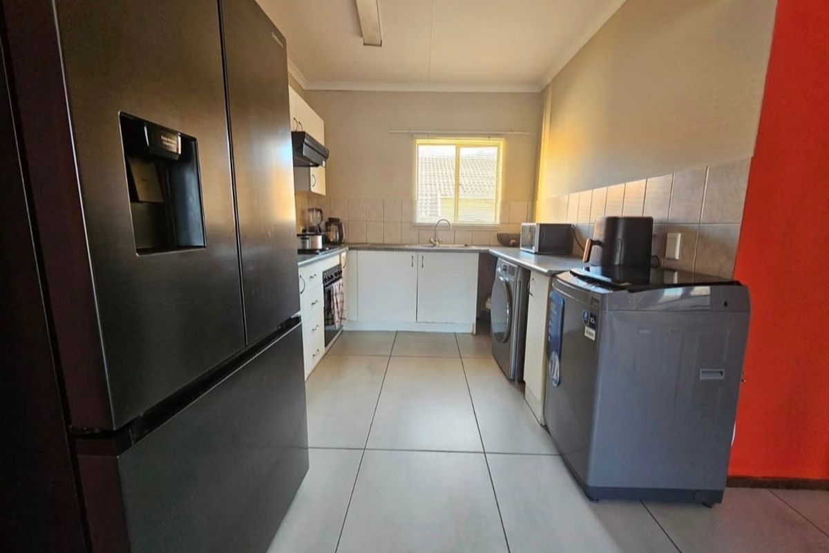 A functional kitchen featuring tiled flooring, built-in cabinetry, a tiled backsplash, and a stainless steel sink with an integrated extractor fan.