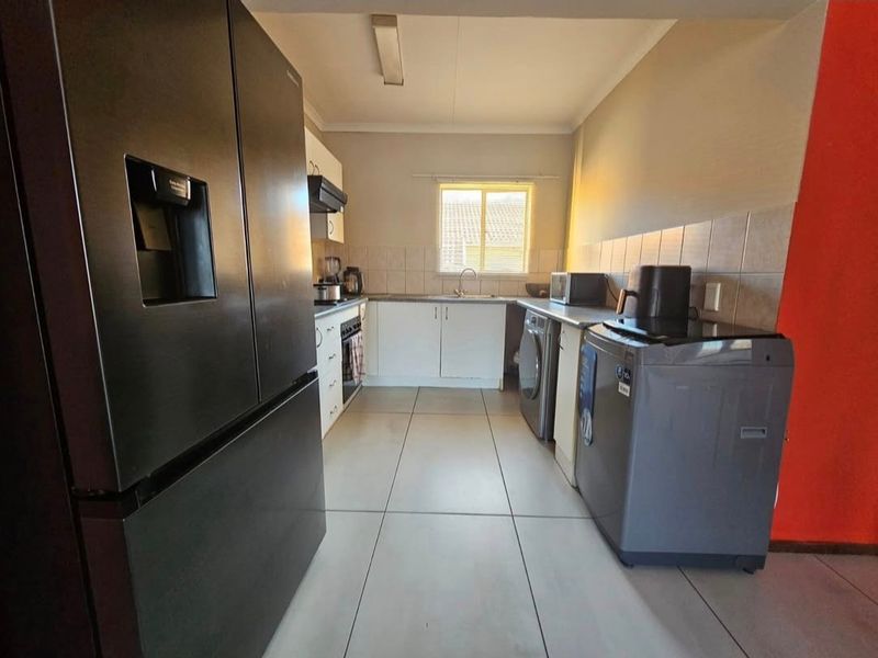 A functional kitchen featuring tiled flooring, built-in cabinetry, a tiled backsplash, and a stainless steel sink with an integrated extractor fan.