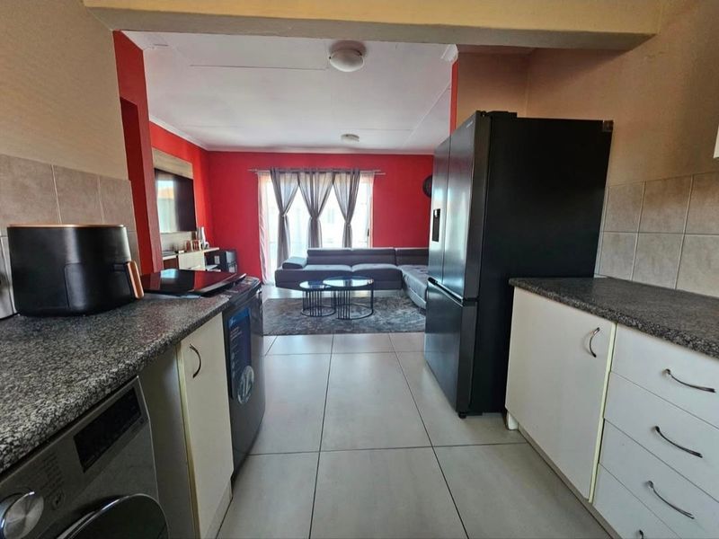 Open-plan living area featuring a functional kitchen with granite countertops and tiled flooring, seamlessly flowing into the adjacent lounge space.