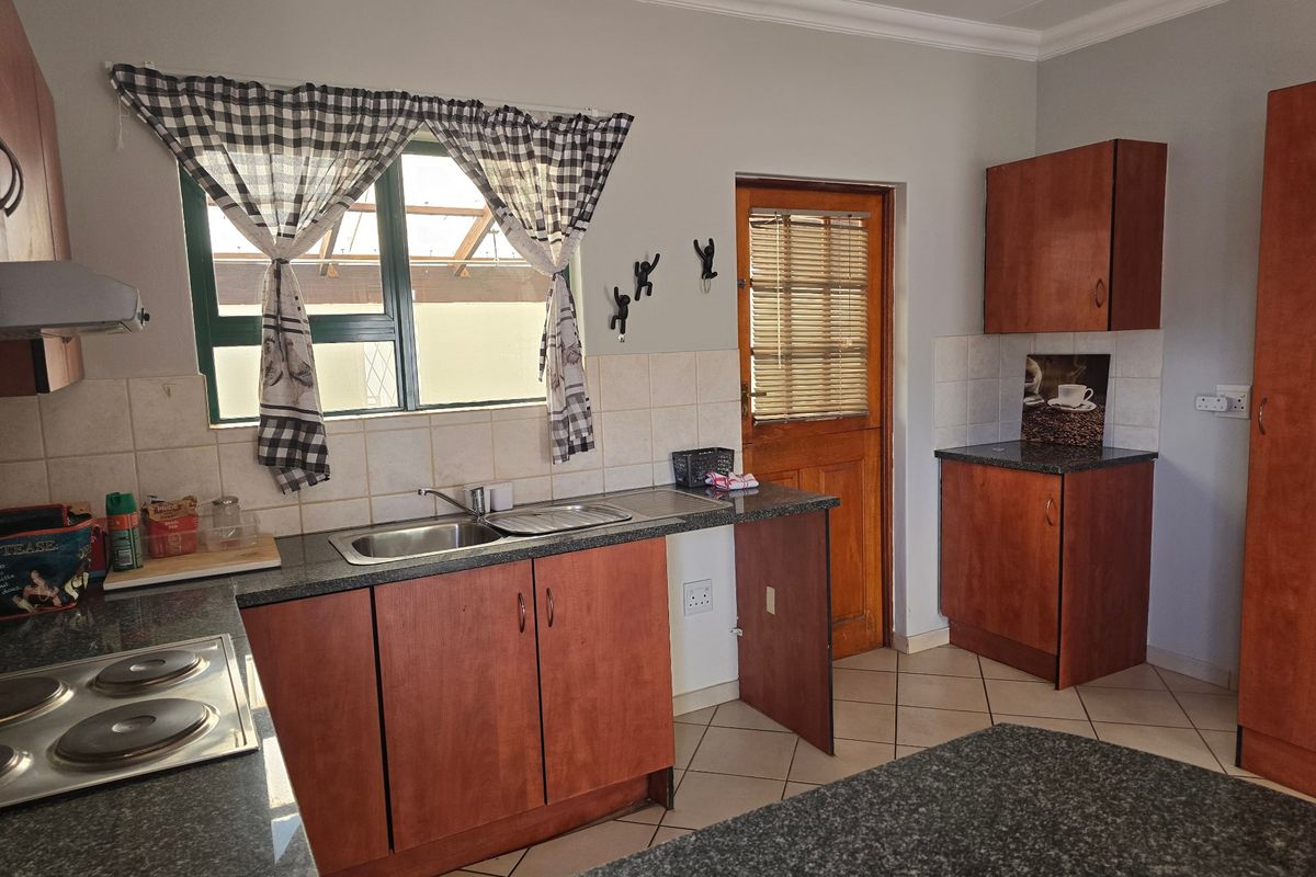 A functional kitchen featuring laminate cabinetry, granite countertops, a double basin sink, and an integrated electric hob with an extractor fan.