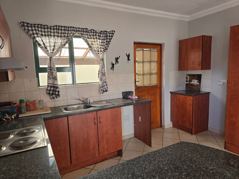 A functional kitchen featuring laminate cabinetry, granite countertops, a double basin sink, and an integrated electric hob with an extractor fan.