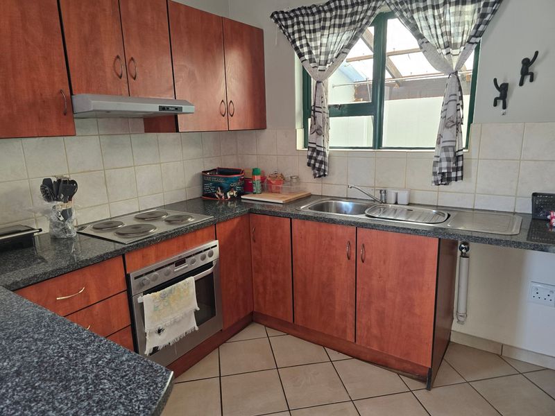 Functional kitchen featuring wood-look cabinetry, granite countertops, built-in oven, electric hob, and tiled backsplash with a window overlooking the exterior.