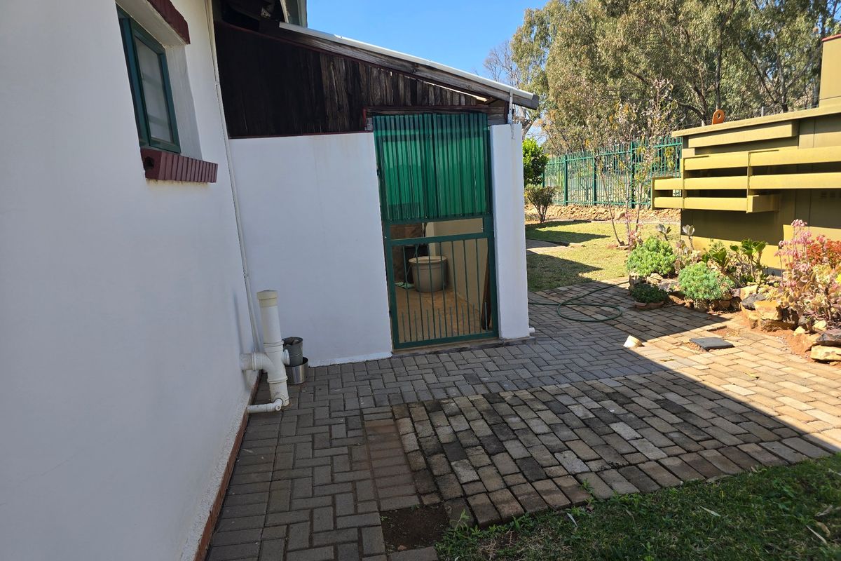 A rear exterior view of the townhouse featuring a paved patio area, security gate access, and external plumbing fixtures.