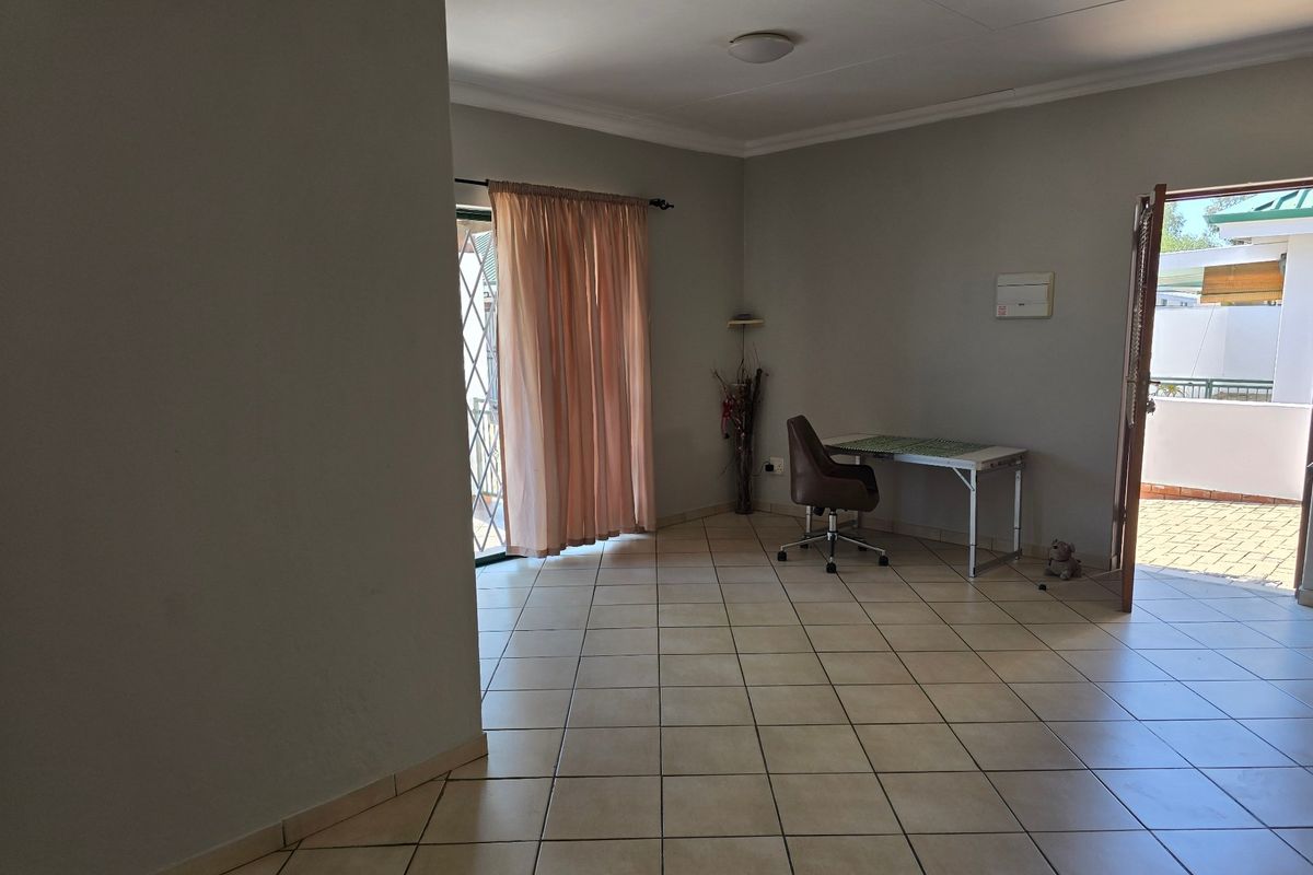 A spacious, tiled living area featuring a sliding door with security gate, providing access to an outdoor patio space.