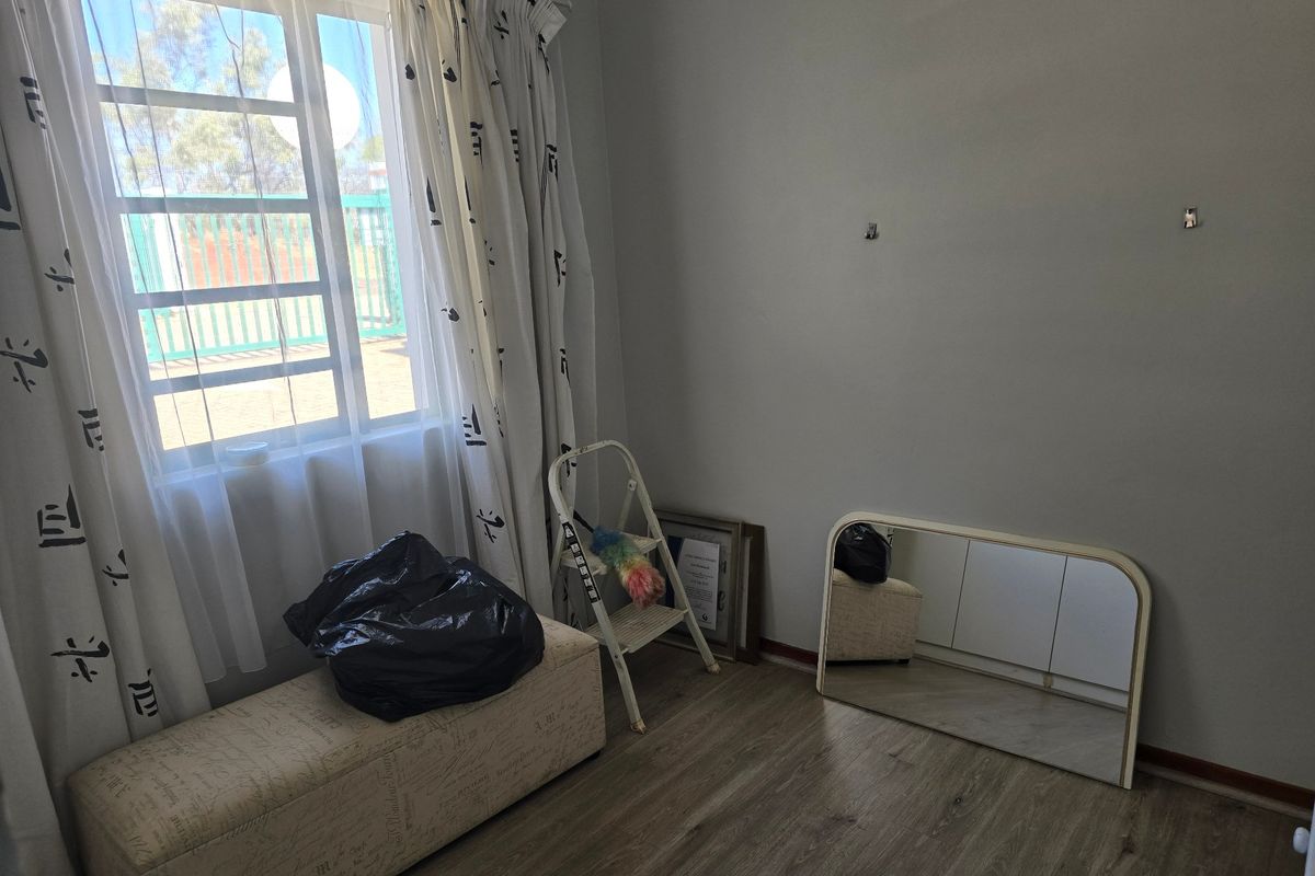A vacant bedroom featuring laminate flooring and a window with security bars, offering a neutral space ready for personalization.