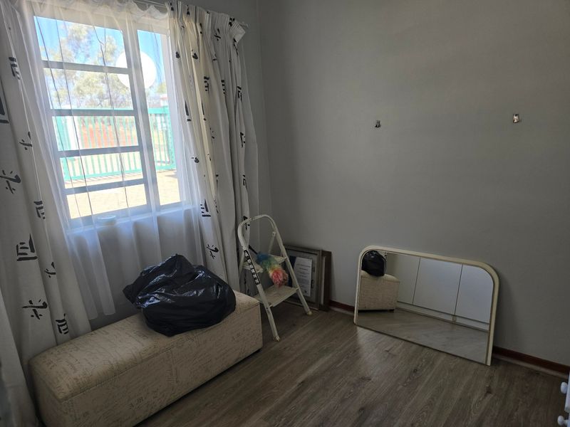 A vacant bedroom featuring laminate flooring and a window with security bars, offering a neutral space ready for personalization.