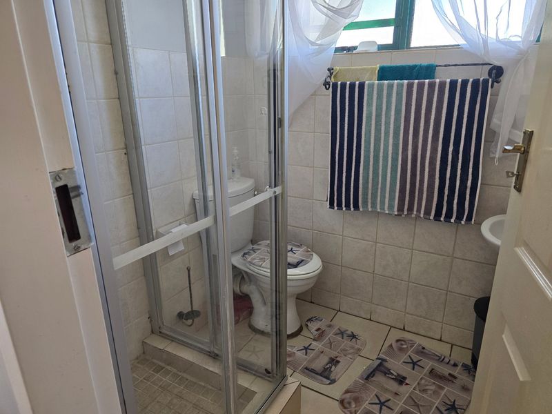 A compact bathroom featuring a shower enclosure, toilet, and tiled finishes, offering a functional layout with natural light from the window.