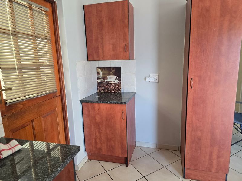 A compact kitchen area featuring wood-finish cabinetry, granite countertops, and tiled flooring, adjacent to a timber door with integrated blinds.