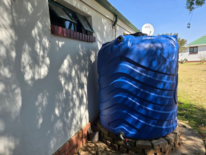 Exterior view of the property featuring a large blue water storage tank mounted on a brick base against the rear wall.