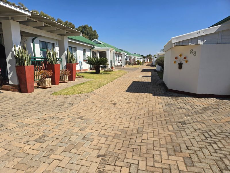 A view of the townhouse complex featuring a paved driveway, covered patios, and well-maintained green metal roofs.