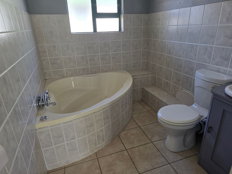 A functional bathroom featuring a corner bathtub, tiled walls and flooring, a standard toilet, and a vanity cabinet.