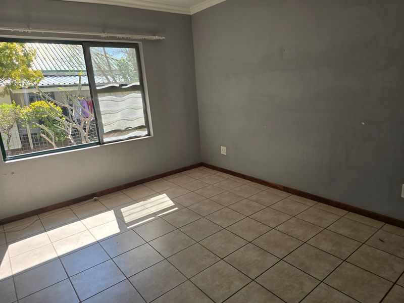 An empty bedroom featuring neutral tiled flooring, grey painted walls, and a sliding window providing natural light.