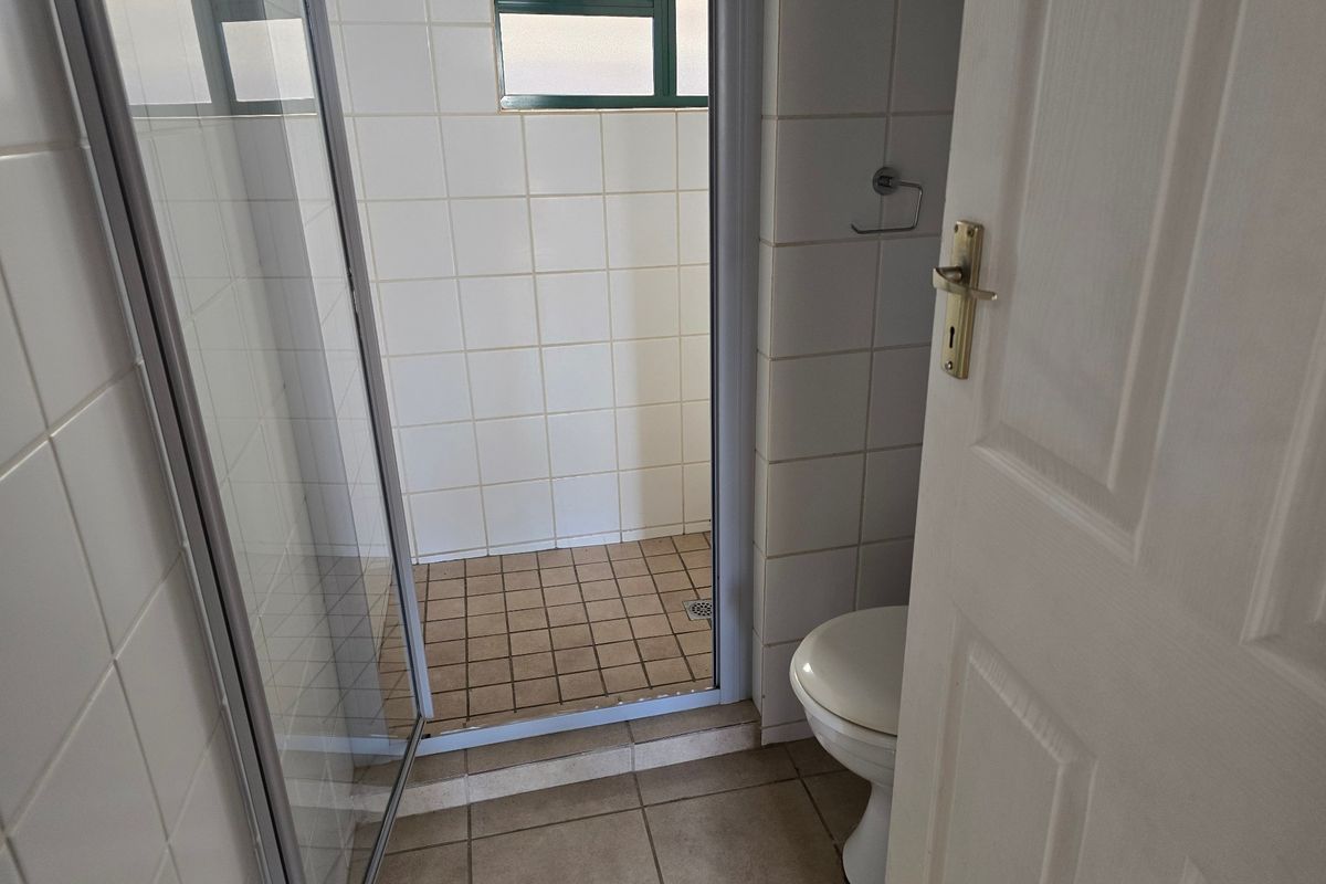A functional bathroom featuring a shower enclosure, toilet, and tiled finishes throughout, presenting a clean but dated aesthetic.
