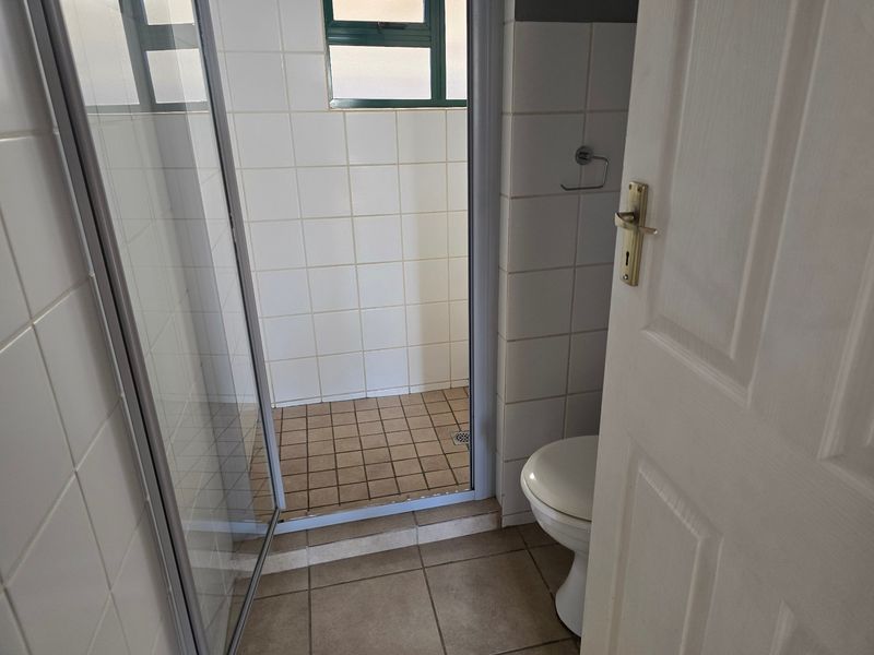 A functional bathroom featuring a shower enclosure, toilet, and tiled finishes throughout, presenting a clean but dated aesthetic.