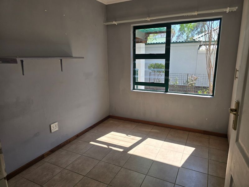 An empty bedroom featuring tiled flooring, a large aluminium window, and a wall-mounted shelf, requiring minor cosmetic updates to the wall finishes.