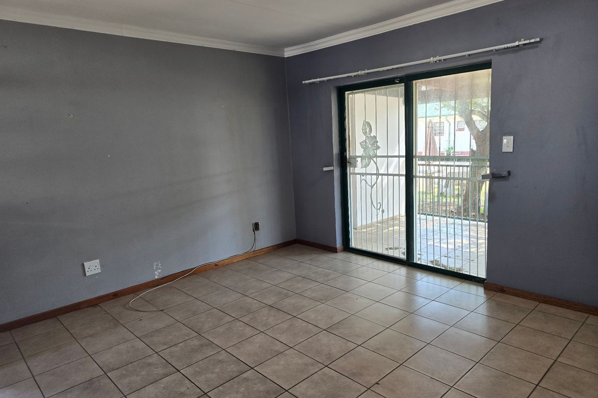 An empty living room featuring tiled flooring, coving, and a sliding glass door with a security gate leading to the exterior.