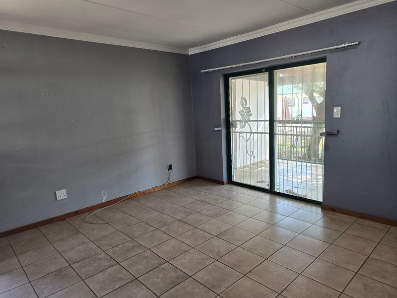 An empty living room featuring tiled flooring, coving, and a sliding glass door with a security gate leading to the exterior.