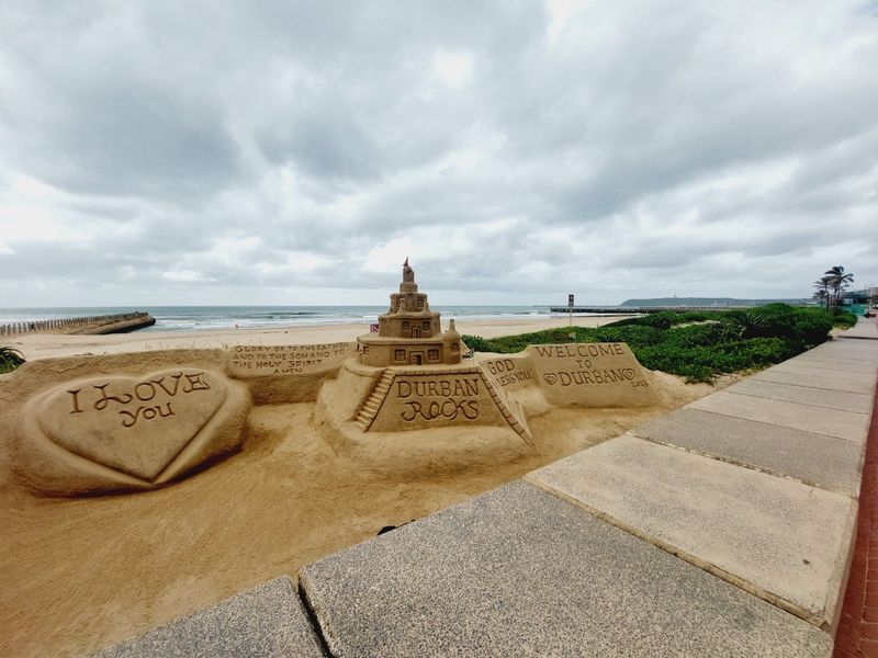 A view of a beach promenade featuring sand sculptures with the ocean in the background.