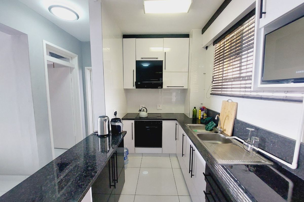 Modern kitchen featuring sleek white cabinetry, contrasting black granite countertops, integrated appliances, and tiled flooring with ample workspace.