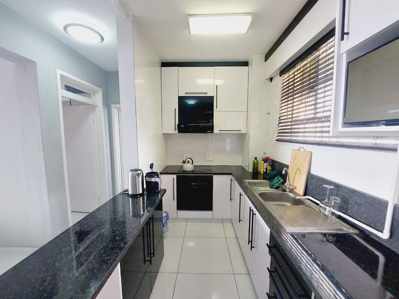 Modern kitchen featuring sleek white cabinetry, contrasting black granite countertops, integrated appliances, and tiled flooring with ample workspace.