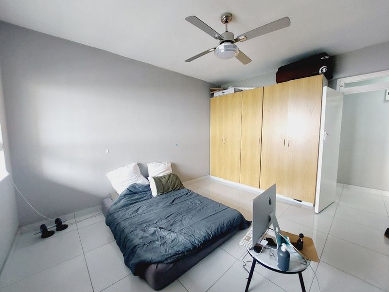 A bedroom featuring tiled flooring, a ceiling fan, and a large built-in wooden wardrobe providing ample storage space.