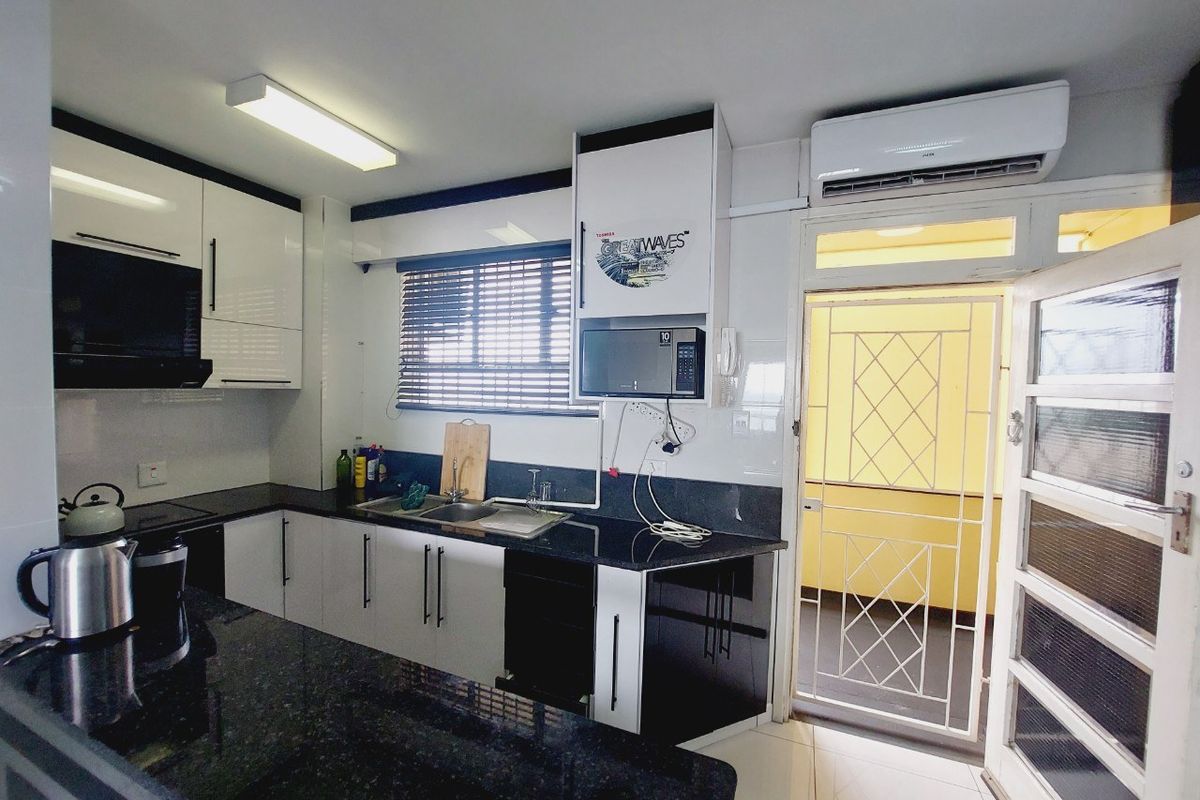 Modern kitchen featuring high-gloss cabinetry, granite countertops, double sink, and integrated extractor fan, with direct access to an outdoor area via a security gate.