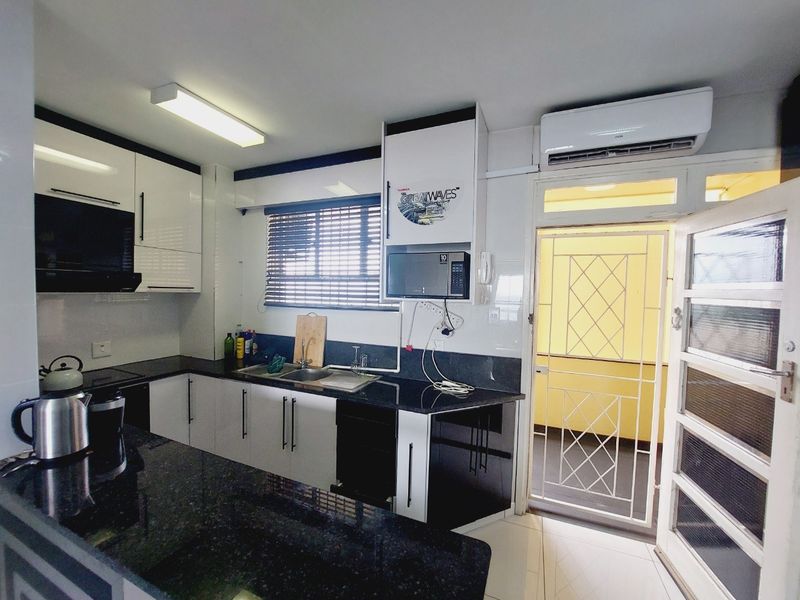 Modern kitchen featuring high-gloss cabinetry, granite countertops, double sink, and integrated extractor fan, with direct access to an outdoor area via a security gate.
