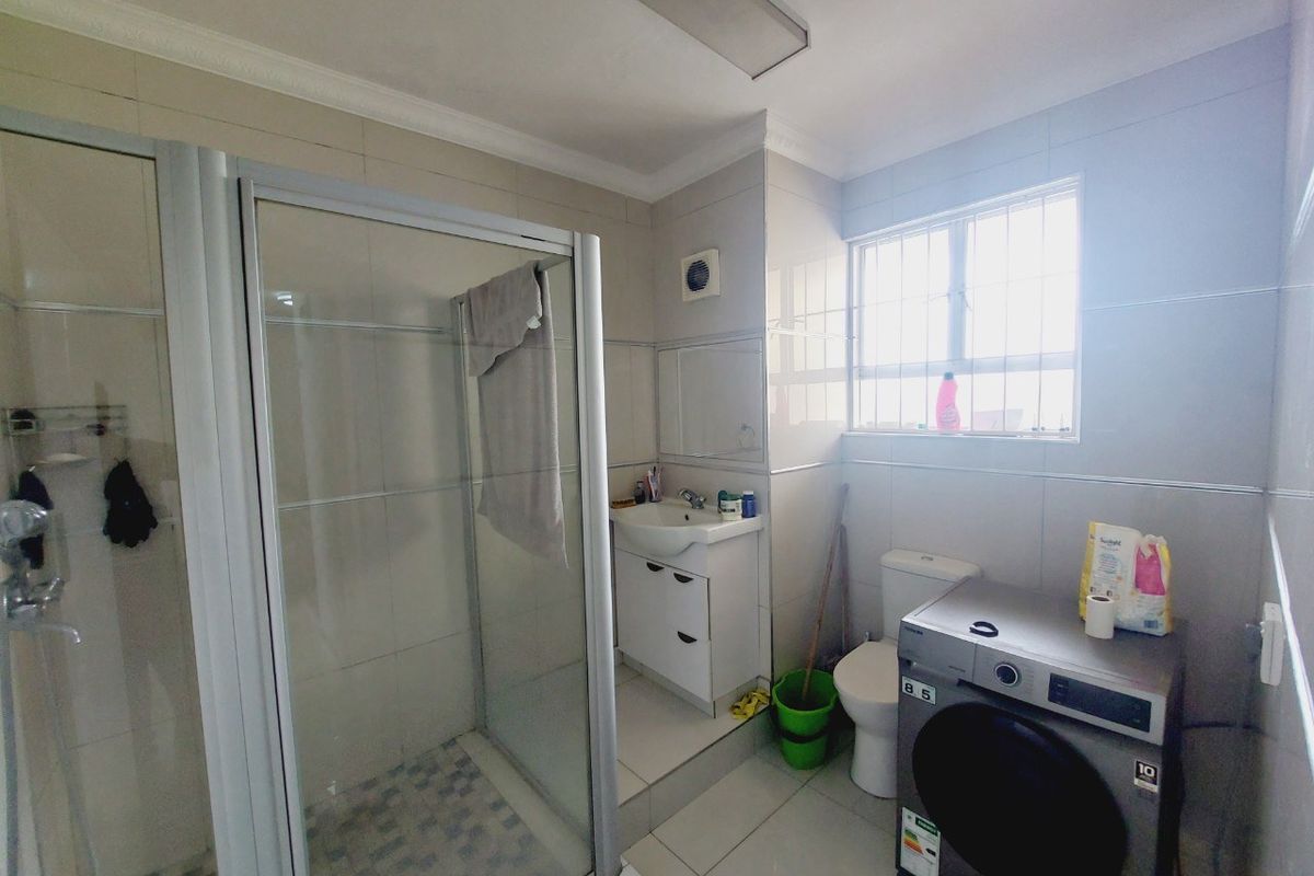 A functional bathroom featuring a glass shower enclosure, vanity basin, toilet, and tiled finishes, with space for laundry appliances.