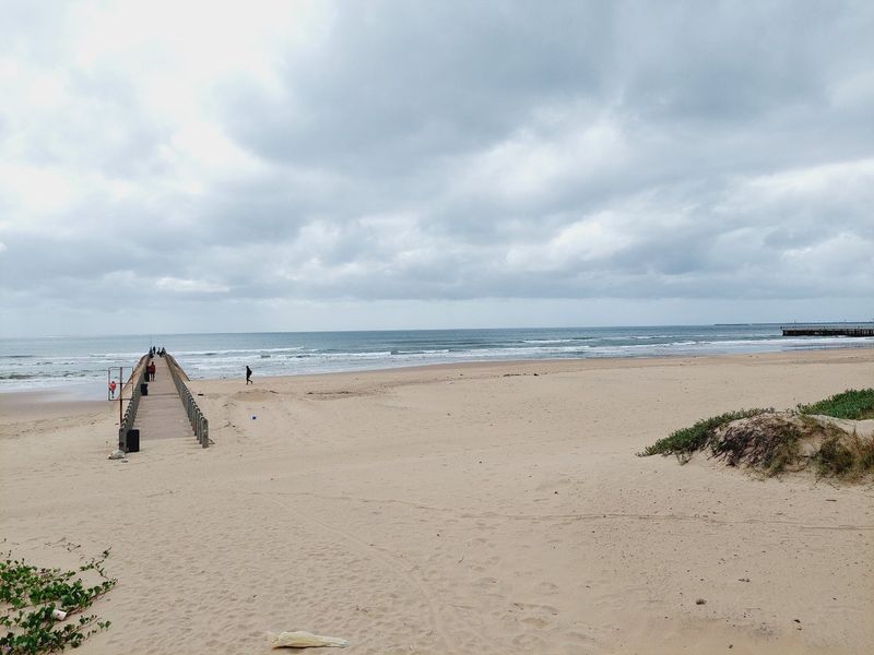 A scenic view of the sandy beach and ocean pier under a cloudy sky.
