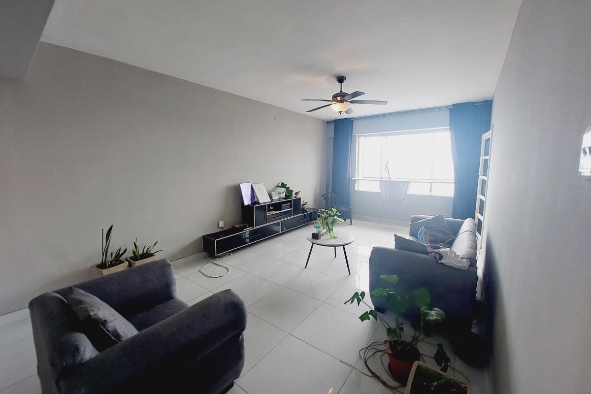 A spacious living room featuring neutral wall tones, large windows for natural light, and polished tiled flooring with a central ceiling fan.