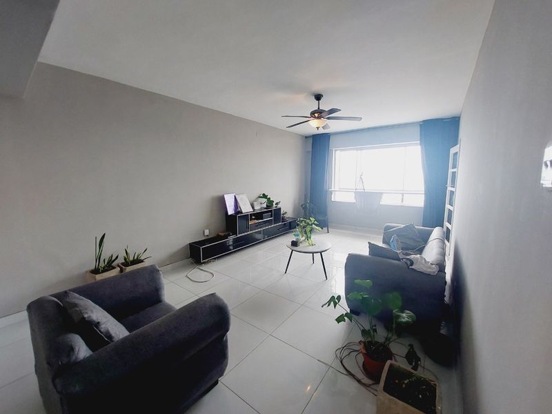 A spacious living room featuring neutral wall tones, large windows for natural light, and polished tiled flooring with a central ceiling fan.