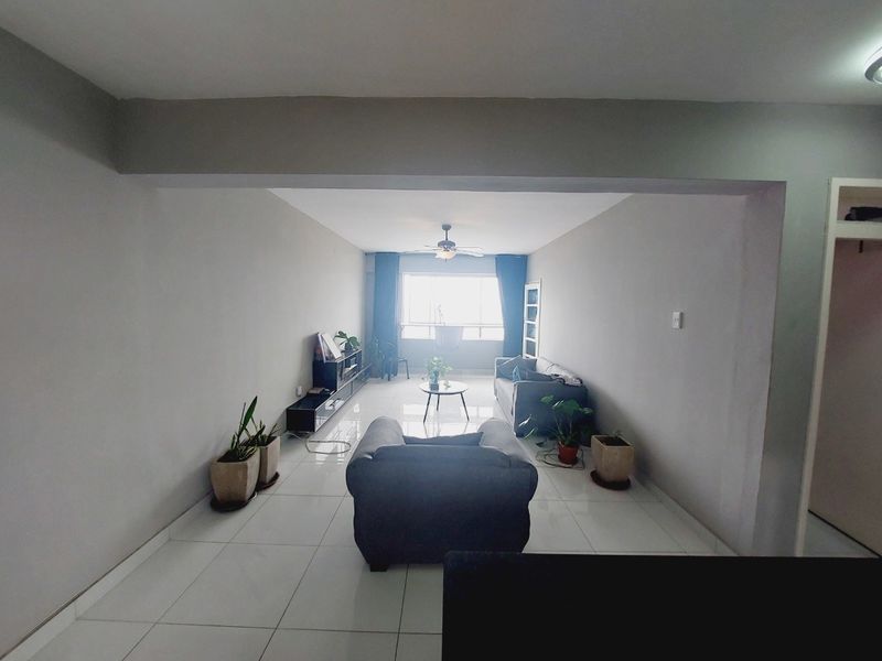 A spacious living room featuring neutral tiled flooring, a ceiling fan, and a large window allowing natural light into the area.